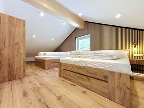Ein modernes Schlafzimmer mit zwei hölzernen Betten, einer geneigten Decke und einem Fenster, das für natürliches Licht sorgt.