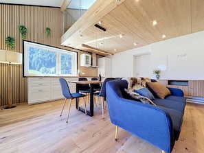 Ein modernes Wohnzimmer mit einem blauen Sofa, Holzboden und einem Essbereich mit Tisch und Stühlen.