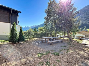 Eine hölzerne Bank und zwei Bäume in einem Garten mit Bergblick.