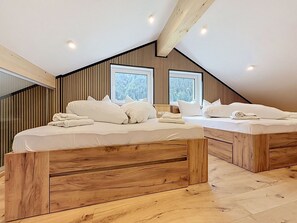 Ein Schlafzimmer mit zwei hölzernen Betten, weißer Bettwäsche und einer schrägen Decke mit Holzbalken.