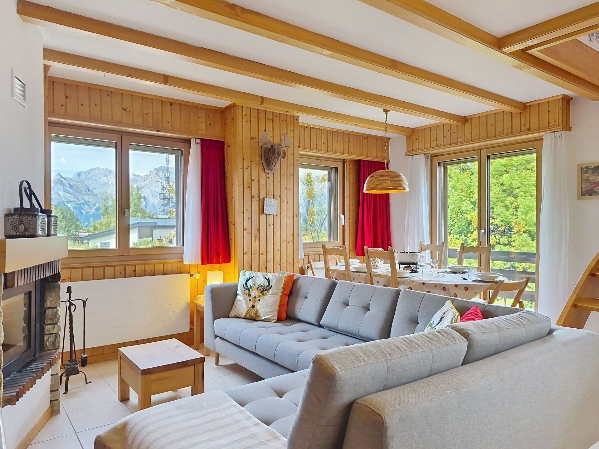 Un salon chaleureux avec une cheminée, un canapé, une table à manger avec des chaises et de grandes fenêtres avec des rideaux.