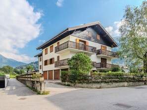 Ein mehrstöckiges Gebäude mit Balkonen, einer gepflasterten Auffahrt und einem Berg im Hintergrund.
