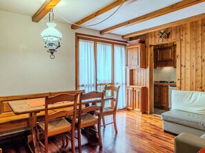A wooden interior with a dining table and chairs, a sofa, a kitchen area, and a hanging light fixture. - Nice apartment for 6 people with WIFI, TV and balcony (Carisolo)