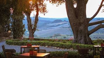 An outdoor seating area with tables and chairs, surrounded by trees and a view of rolling hills.