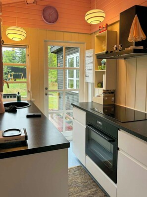 A kitchen with a built-in oven, a sink, and a window overlooking a garden. - Summer house in pastel shades near Ebeltoft (Ebeltoft)