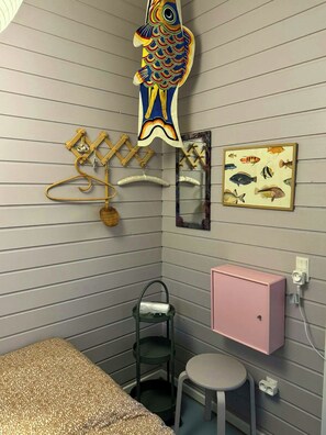 A room with a bed, a small stool, a pink cabinet, a fish decoration, a mirror, and a framed fish illustration on the wall. - Summer house in pastel shades near Ebeltoft (Ebeltoft)
