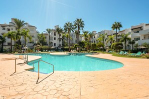 A swimming pool with a tiled deck, surrounded by palm trees and lounge chairs. - RDR586 - Tropical 2-Bed Apartment with Pool Views (Estepona)