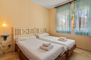 A hotel room with two beds, a nightstand, a lamp, and a window with curtains. - RDR586 - Tropical 2-Bed Apartment with Pool Views (Estepona)