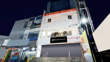 Um edifício de vários andares com uma loja fechada no andar térreo, uma escadaria que leva aos andares superiores e uma placa indicando 'OYO TOWNHOUSE'.