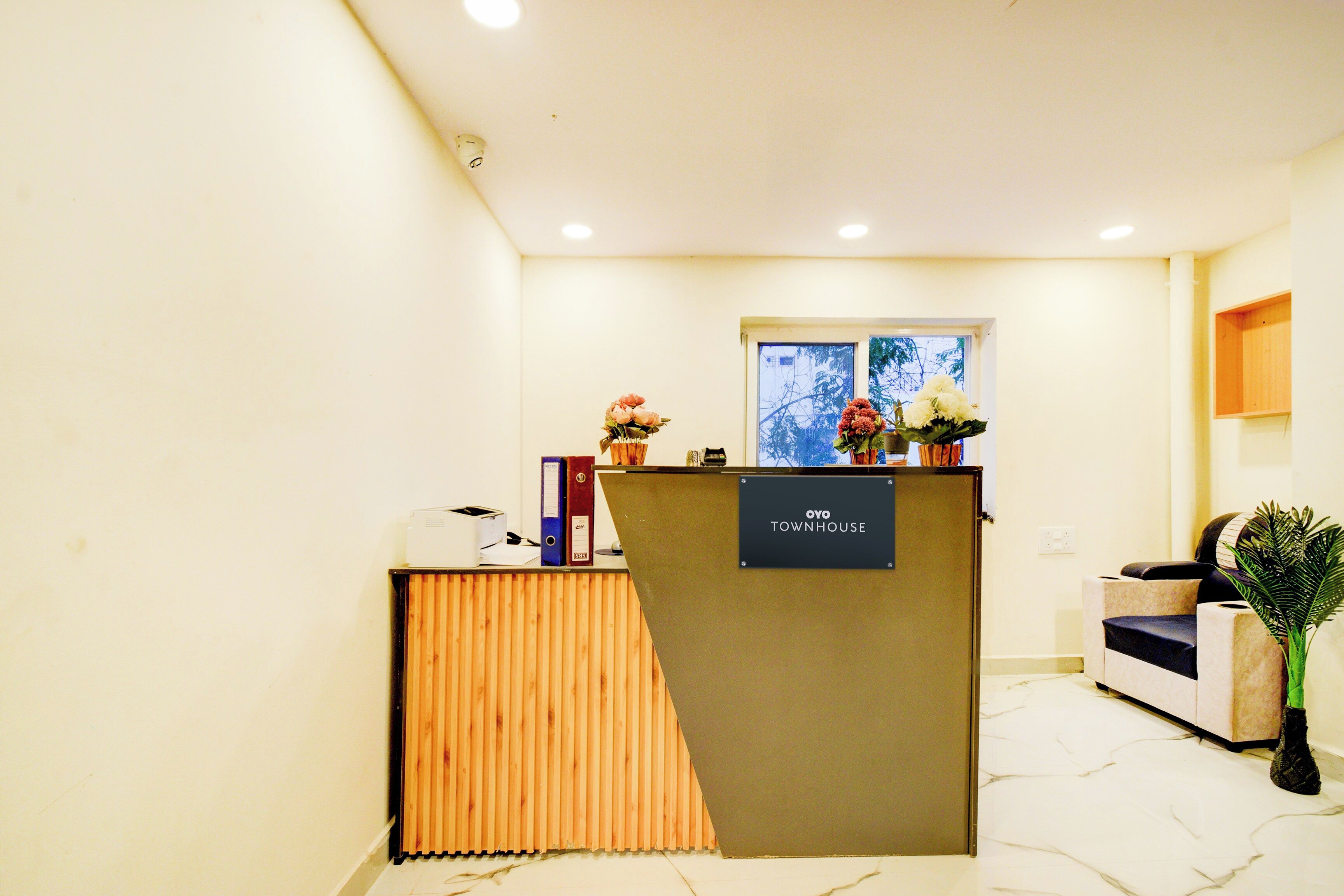 A reception desk with a sign reading 'OYO TOWNHOUSE,' a window with a view of trees, and a potted plant.