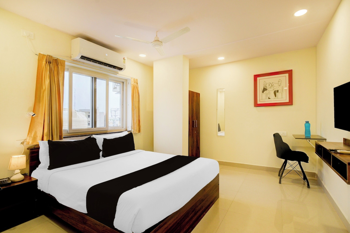 Una habitación de hotel con cama, escritorio con silla, televisión y ventana con cortinas.
