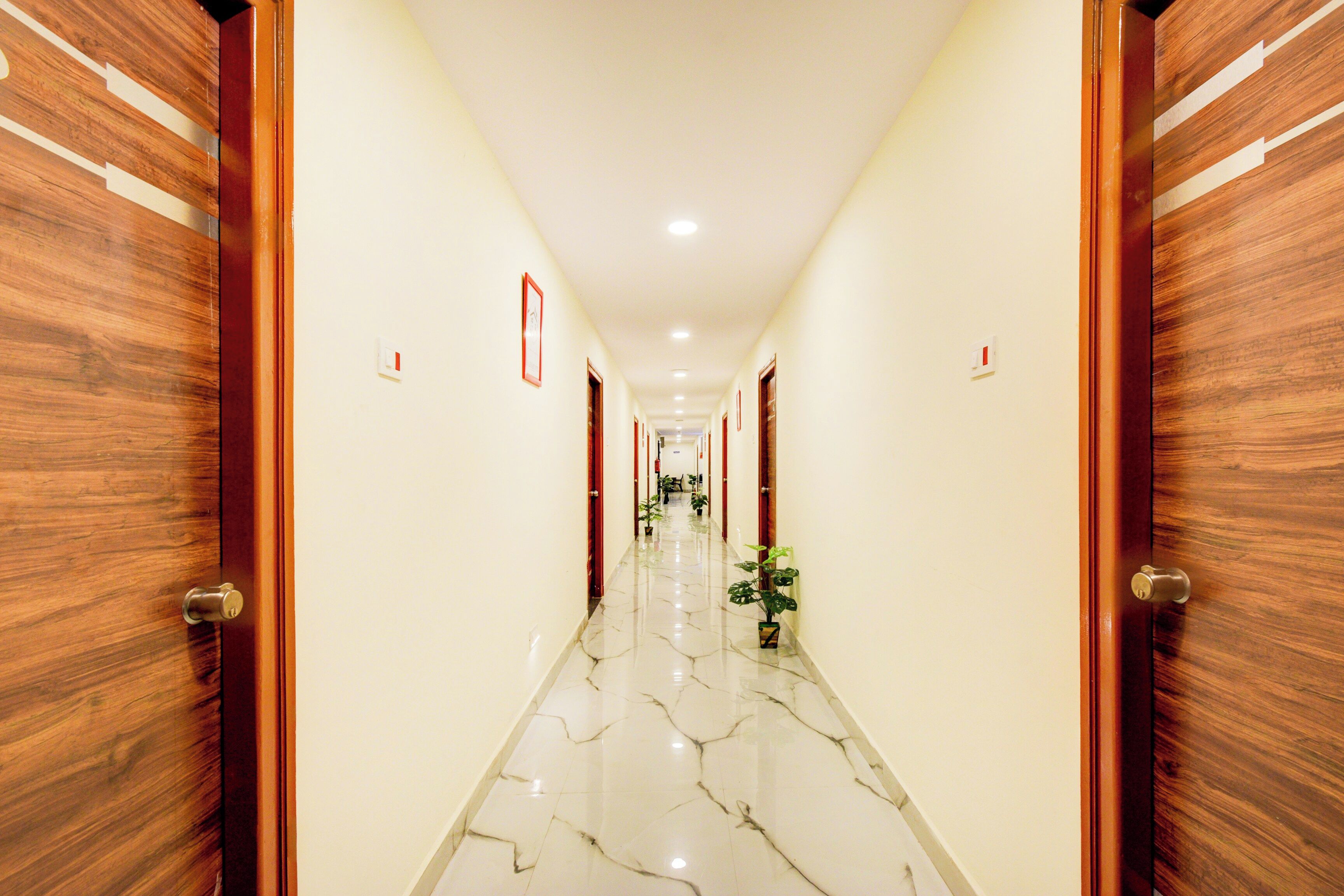 Un pasillo de hotel con puertas de madera, paredes blancas y suelo de mármol.