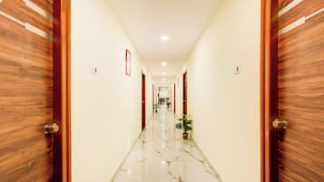 Un pasillo de hotel con puertas de madera, paredes blancas y suelo de mármol.