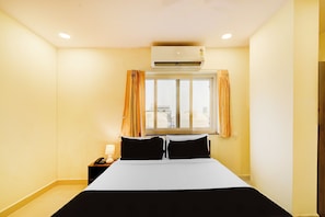Habitación de hotel con cama, ventana con cortinas, equipo de aire acondicionado y teléfono en la mesita de noche.