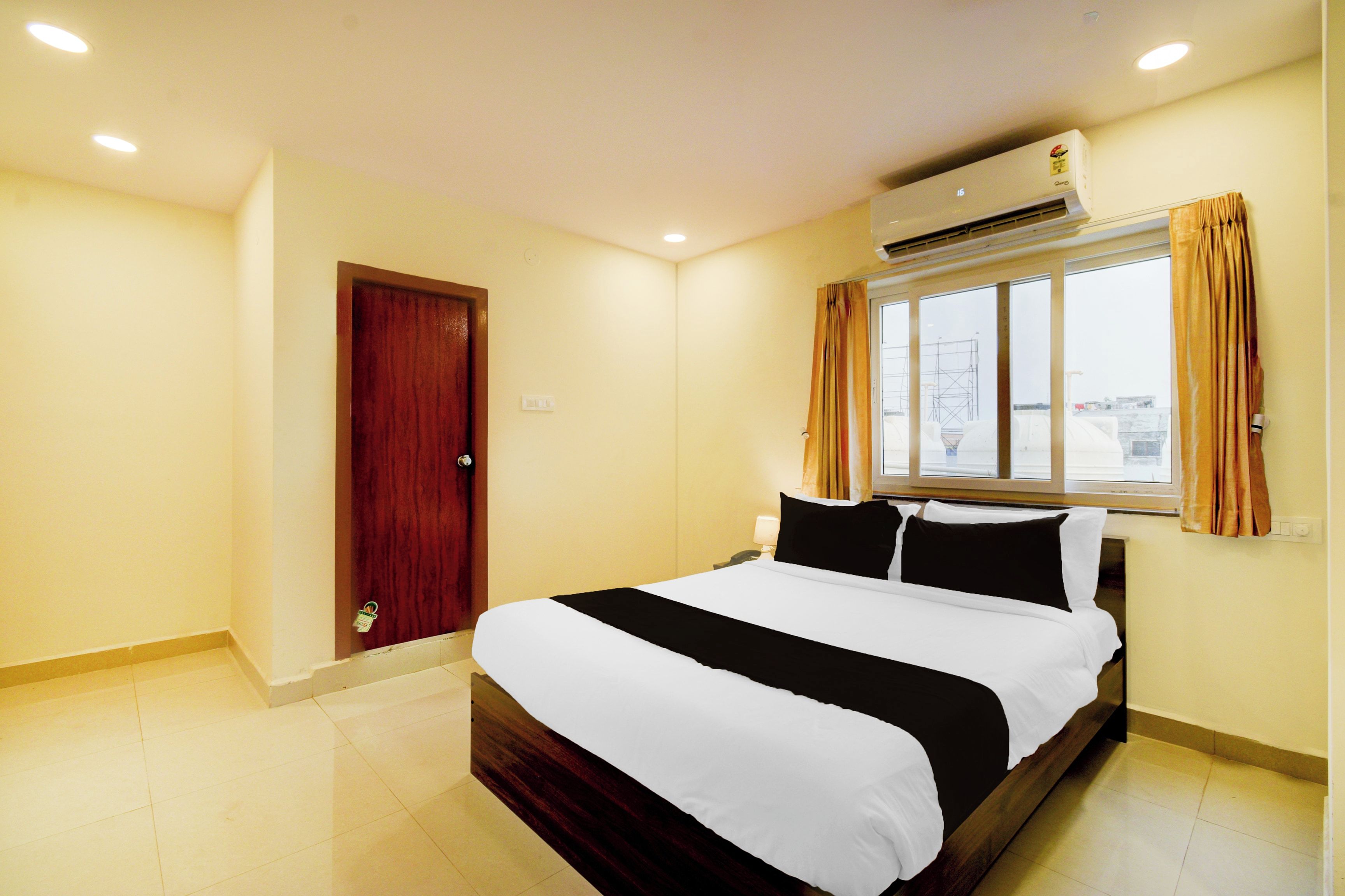 Quarto de hotel com uma cama, ar-condicionado, janela com cortinas e uma porta.