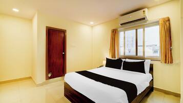 Quarto de hotel com uma cama, ar-condicionado, janela com cortinas e uma porta.