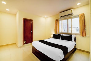 Quarto de hotel com uma cama, ar-condicionado, janela com cortinas e uma porta.