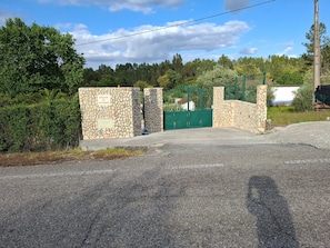 En lukket indgang med en stenvæg og en grøn port, omgivet af vegetation og træer.
