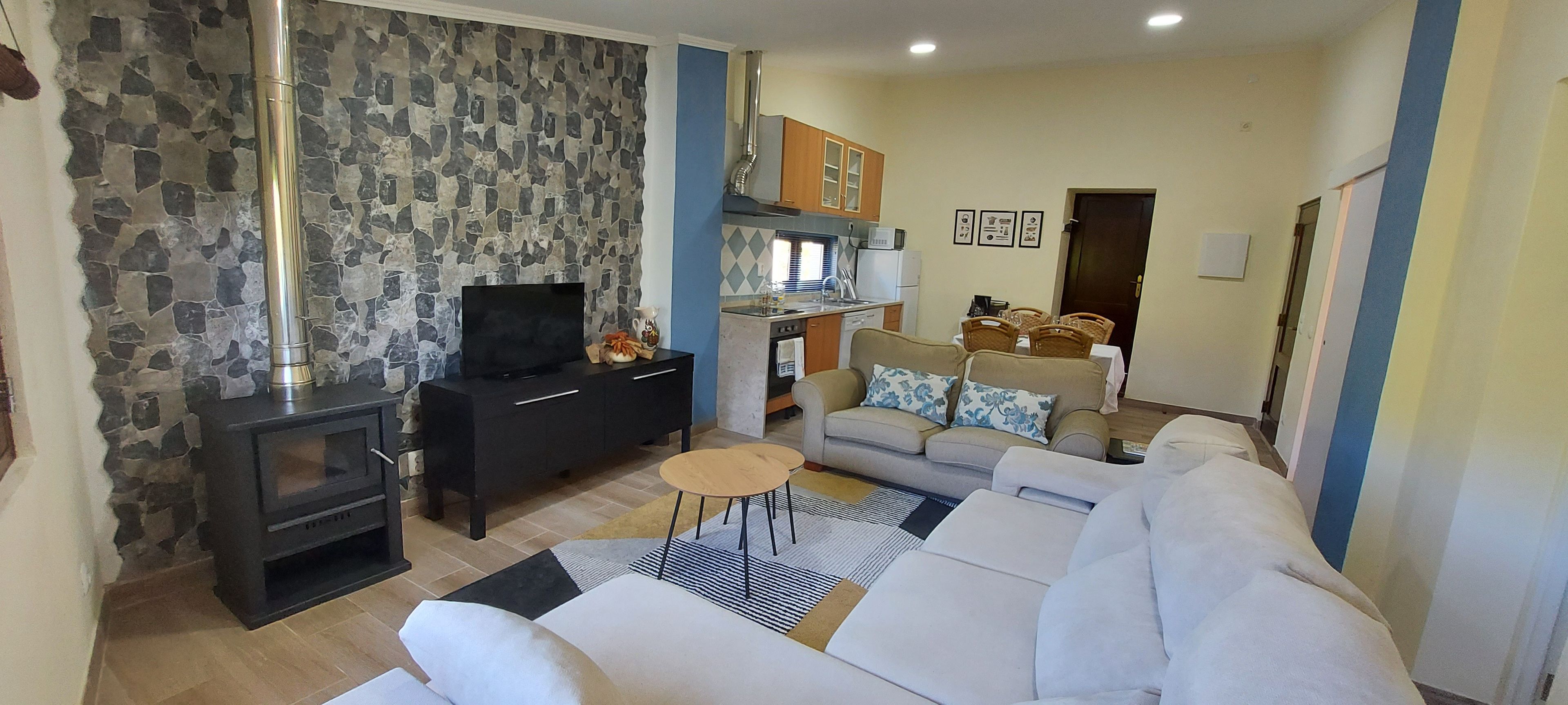 A living room with a fireplace, a sofa, a TV, and a kitchen area with cabinets and a dining table.