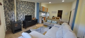 A living room with a fireplace, a sofa, a TV, and a kitchen area with cabinets and a dining table.