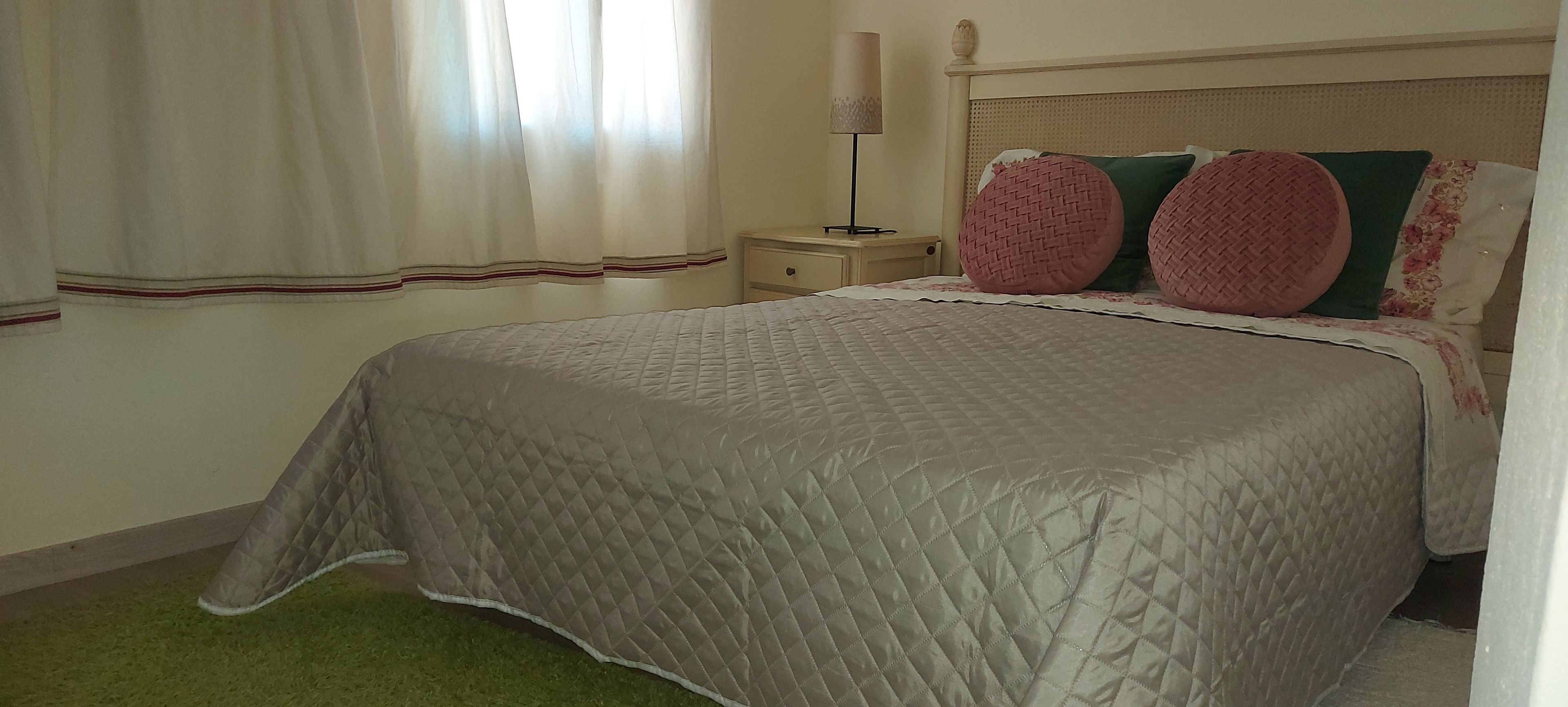 Ein Schlafzimmer mit einem Bett, einem Nachttisch, einer Lampe und einem Fenster mit Vorhängen.