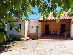A two-story building with a stone facade, a red-tiled roof, and a covered patio area with outdoor seating.