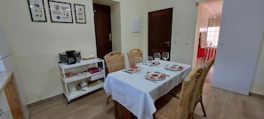 A dining area with a table set for four, chairs, a coffee station, and framed pictures on the wall.