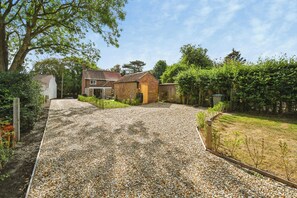 A gravel driveway leading to a brick house with a tiled roof, surrounded by greenery and trees. - Susans Cottage (Horncastle)
