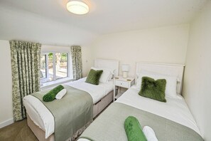 A hotel room with two beds, a window with curtains, a bedside table with a lamp, and a headboard. - Susans Cottage (Horncastle)