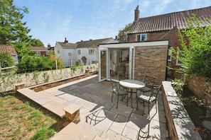 Une terrasse avec une table et des chaises, un mur en briques et un espace jardin.