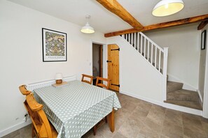 A dining area with a table and chairs, a staircase, and a door. - Susans Cottage (Horncastle)
