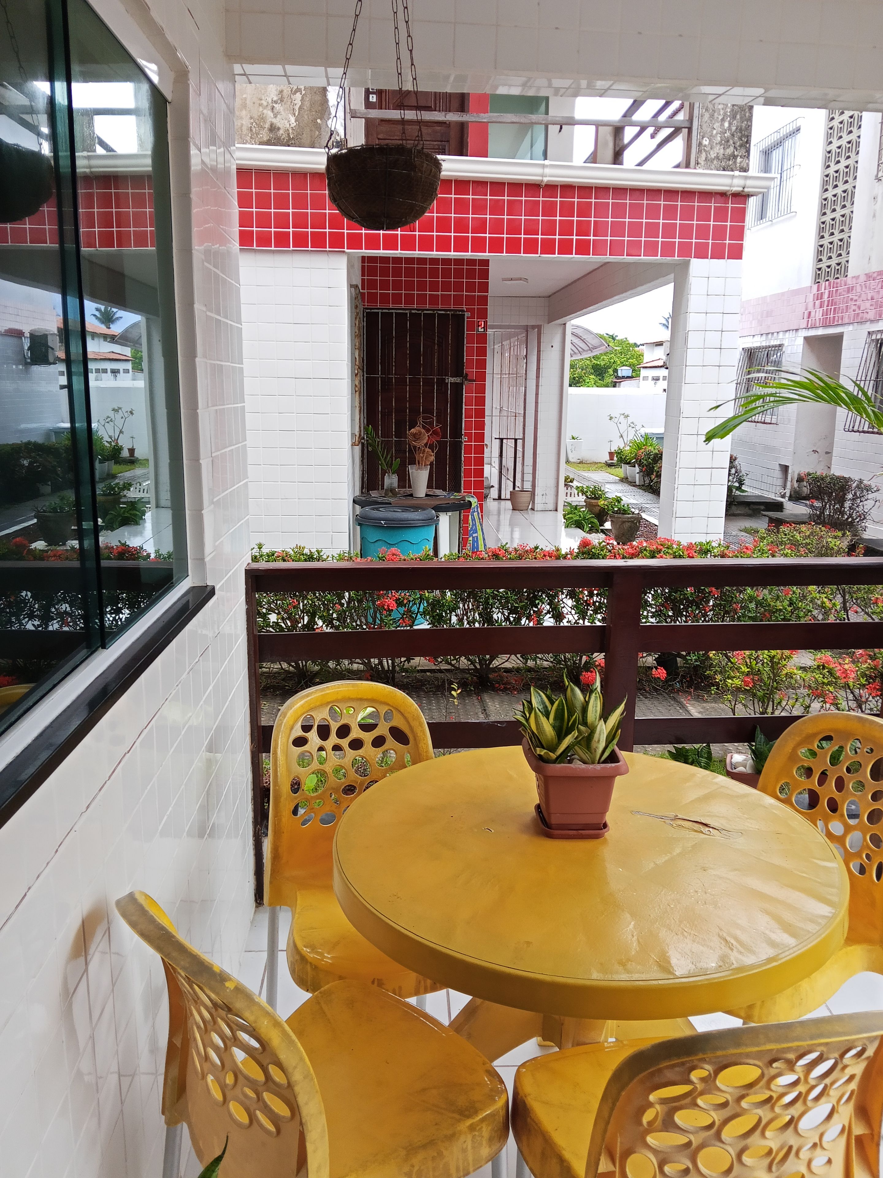 A yellow table with four chairs, a hanging basket, and a potted plant on the table.