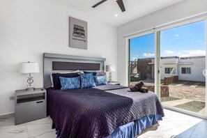 A modern bedroom with a large bed, a headboard, a nightstand, a lamp, and a view of the outside. - Dog-friendly Retreat With Ocean-view Rooftop Deck, Pool, hot Tub, & Kitchen (Playas de Rosarito)