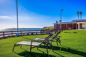 A grassy area with lounge chairs, a view of the ocean, and a building with solar panels. - Dog-friendly Retreat With Ocean-view Rooftop Deck, Pool, hot Tub, & Kitchen (Playas de Rosarito)