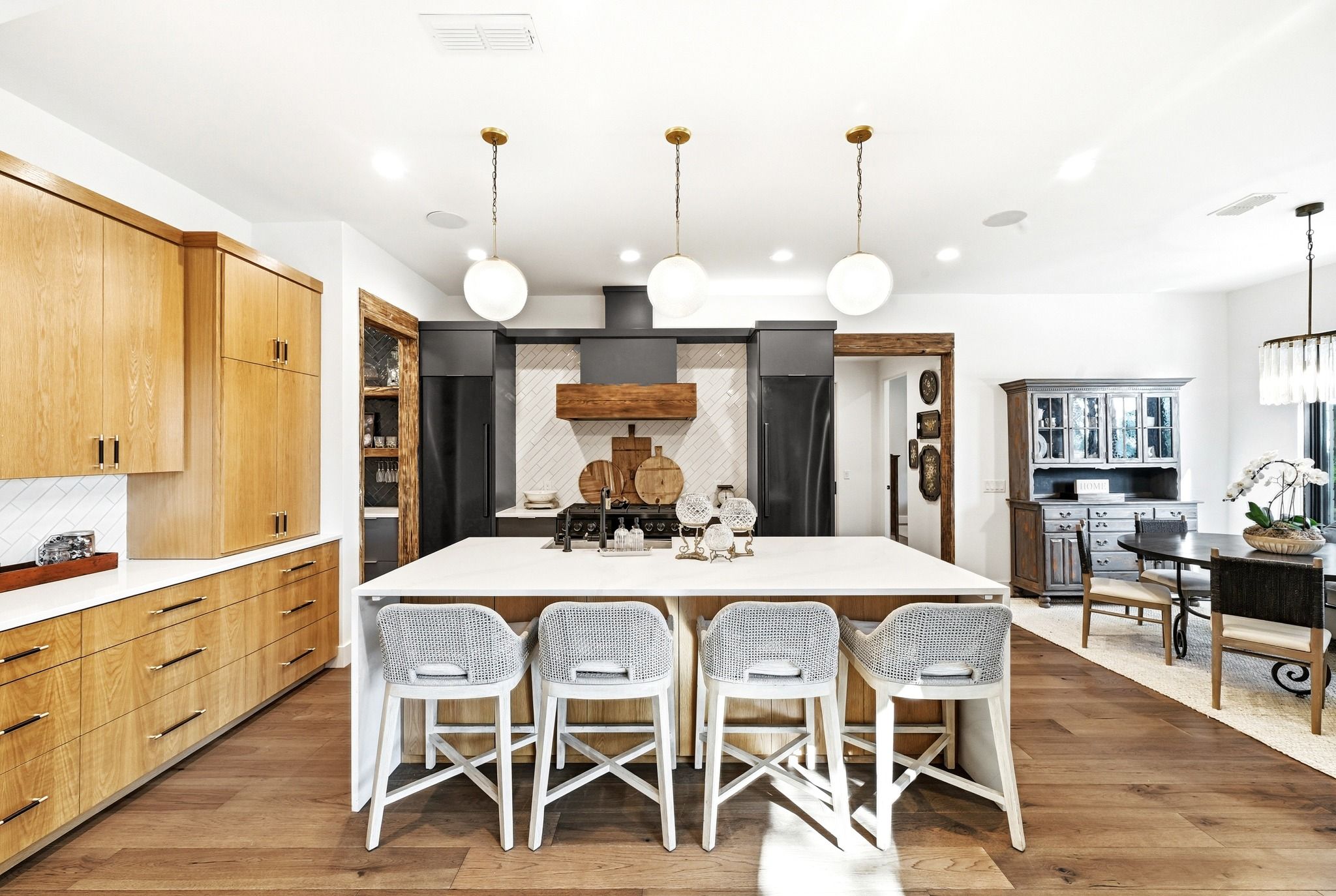 A modern kitchen with a central island, wooden cabinets, and a dining area with white chairs.