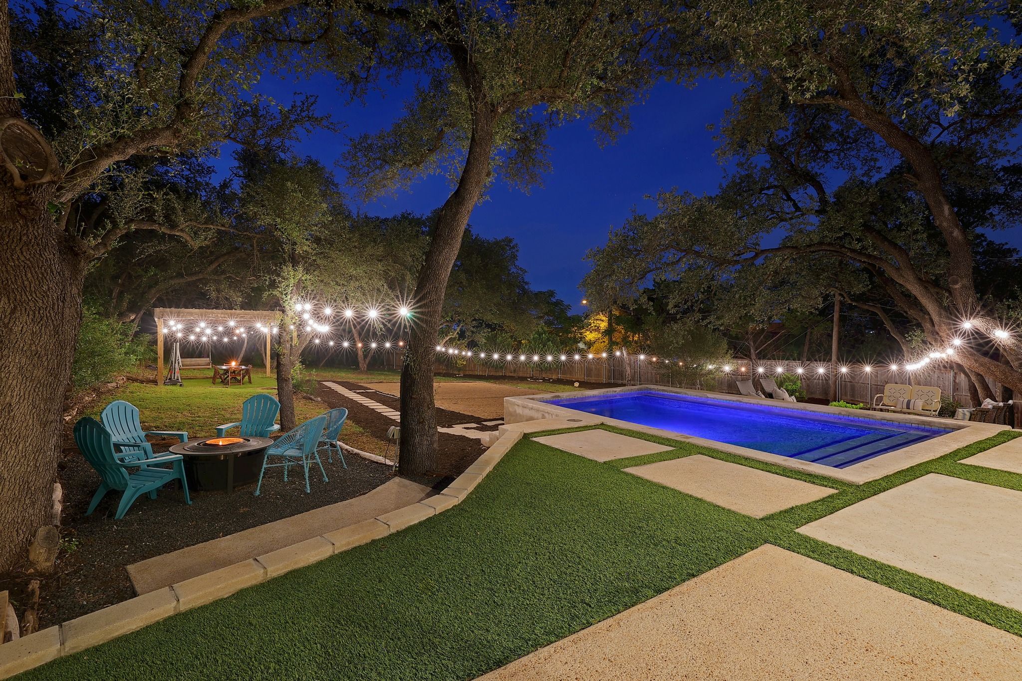 A backyard with a swimming pool, outdoor seating, and string lights.