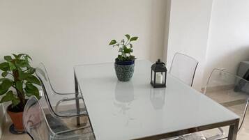 Un espace repas moderne avec une table en verre, des chaises en métal, un vase à motifs, une plante en pot et un luminaire suspendu.