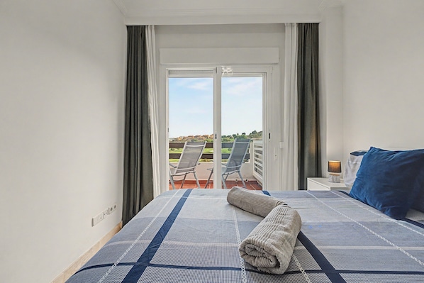 A hotel room with a bed, a nightstand, a lamp, a window with curtains, and a view of the outside.