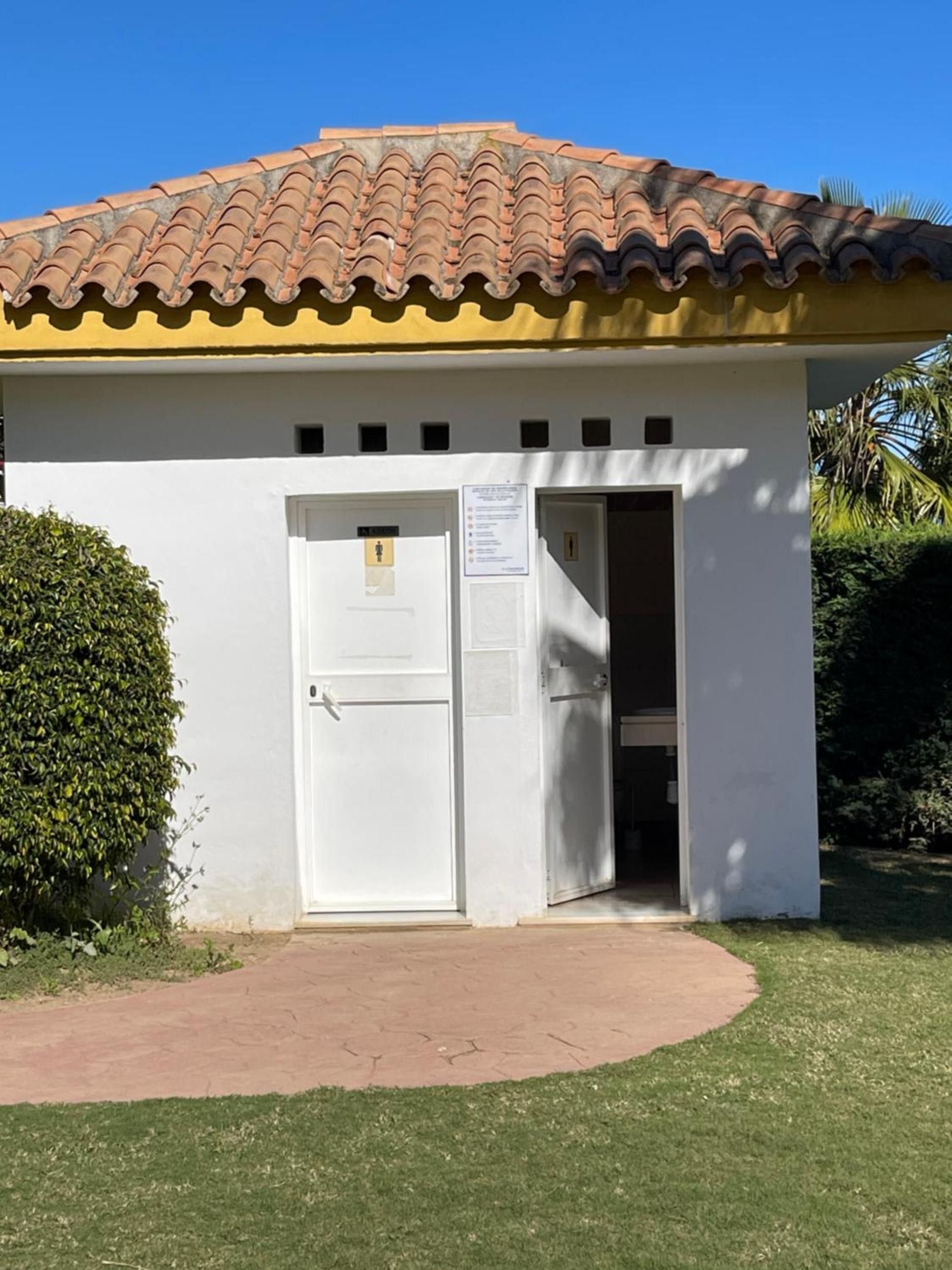 Un petit bâtiment avec un toit en tuiles, une façade blanche et une porte sur laquelle est apposée une enseigne.
