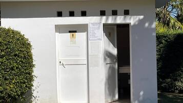 Un petit bâtiment avec un toit en tuiles, une façade blanche et une porte sur laquelle est apposée une enseigne.
