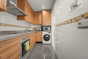A modern kitchen with wooden cabinets, a built-in oven, a microwave, and a washing machine.