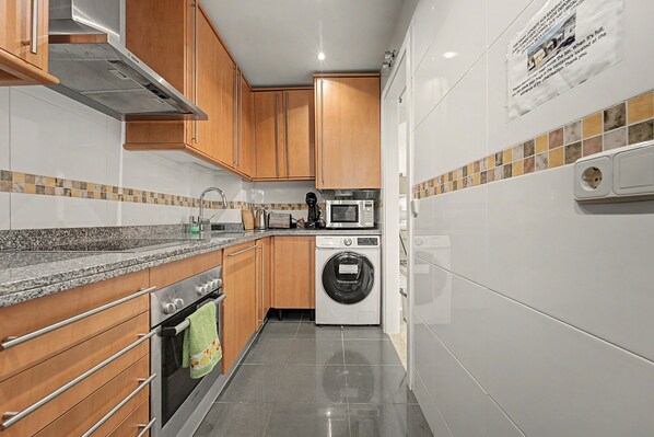A modern kitchen with wooden cabinets, a built-in oven, a microwave, and a washing machine.