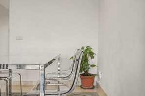 A clear glass table with chairs, a potted plant, and a white wall.