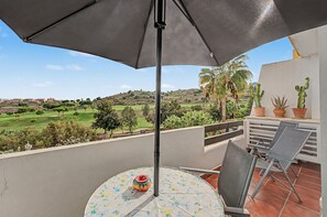 A balcony with a table, chairs, and a potted plant.