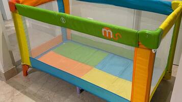 Un parc pour enfants aux couleurs vives, doté d’un sommet en tissu à mailles, placé dans un couloir dont le sol est carrelé et les murs peints en blanc.