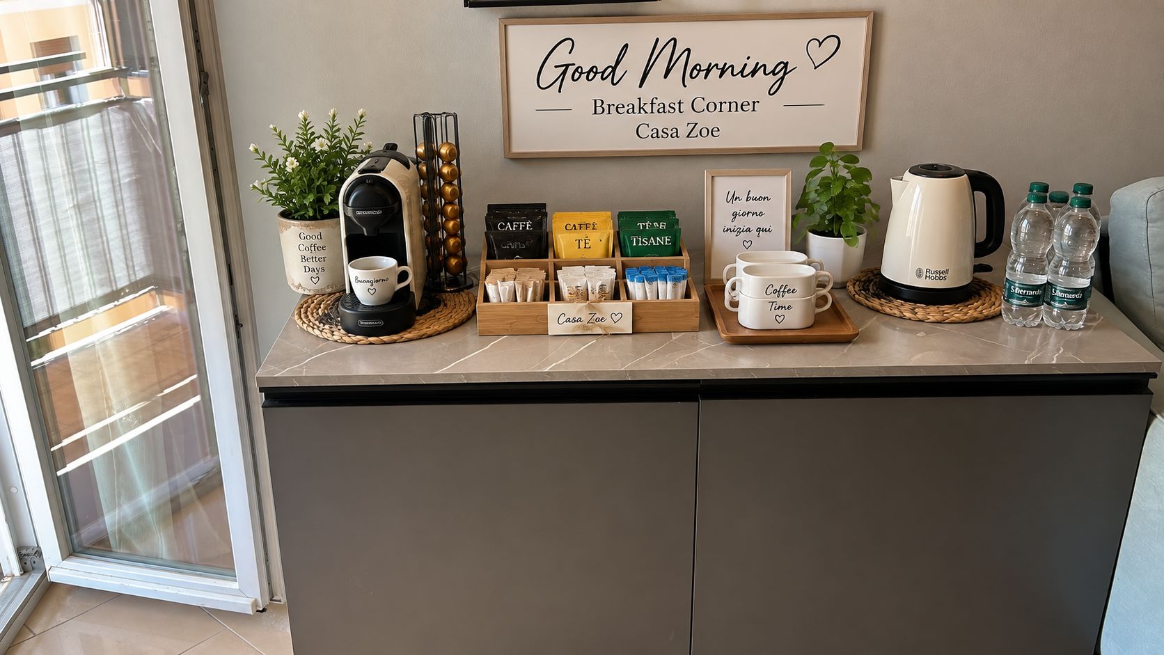 Un angolo colazione con una macchina da caffè, cialde per caffè e tè, un cartello incorniciato e un bollitore su un piano di lavoro.
