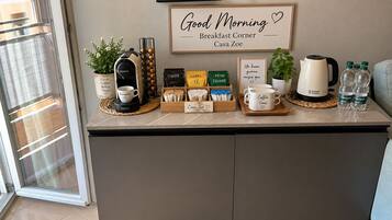 Un angolo colazione con una macchina da caffè, cialde per caffè e tè, un cartello incorniciato e un bollitore su un piano di lavoro.