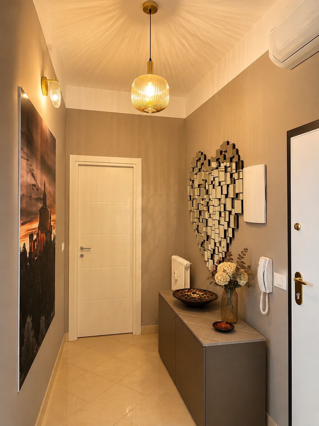 A hallway with a white door, a wall-mounted light fixture, a decorative wall art piece, and a telephone on a console table.