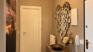 A hallway with a white door, a wall-mounted light fixture, a decorative wall art piece, and a telephone on a console table.