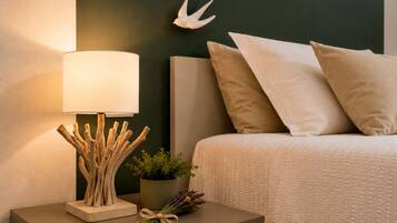Un lit bien fait, avec une tête de lit blanche, une lampe de chevet à la base en bois et une petite plante en pot posée sur la table de chevet.